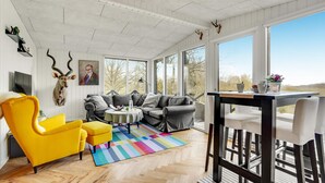 Una habitación amplia con un gran ventanal, un sofá, un sillón amarillo y una mesa de comedor.