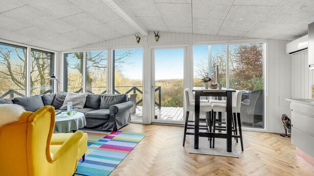 Una sala de estar moderna con un sofá, una silla amarilla, una mesa de comedor con sillas y una alfombra colorida.