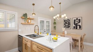 Een moderne keuken met een centraal eiland, houten keukenkastjes, een inbouwvaatwasser en hangende lampen.