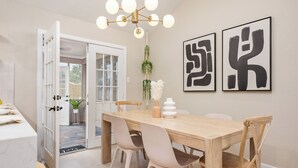 Een eetgedeelte met een houten tafel, vier stoelen, een kroonluchter en twee abstracte kunstwerken aan de muur.