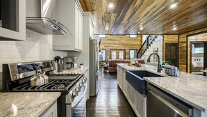 A modern kitchen with stainless steel appliances, a wooden ceiling, and a central island. - Greyhawk Pines|Sleeps16|HotTub|Arcade|Shuffleboard (Broken Bow)