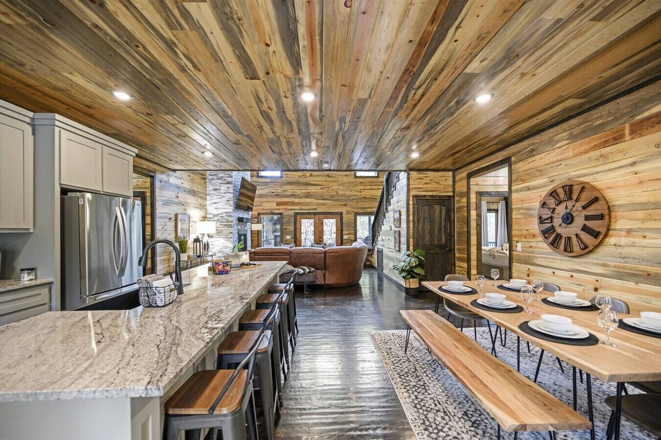 A modern kitchen with a large island, wooden ceiling, and a dining area with a wooden table and benches.
