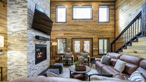 A spacious living room with a fireplace, leather sofa, and a staircase. - Greyhawk Pines|Sleeps16|HotTub|Arcade|Shuffleboard (Broken Bow)