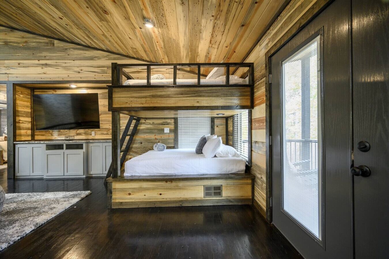 A bunk bed with a TV in the headboard, a wooden ceiling, and a large window.