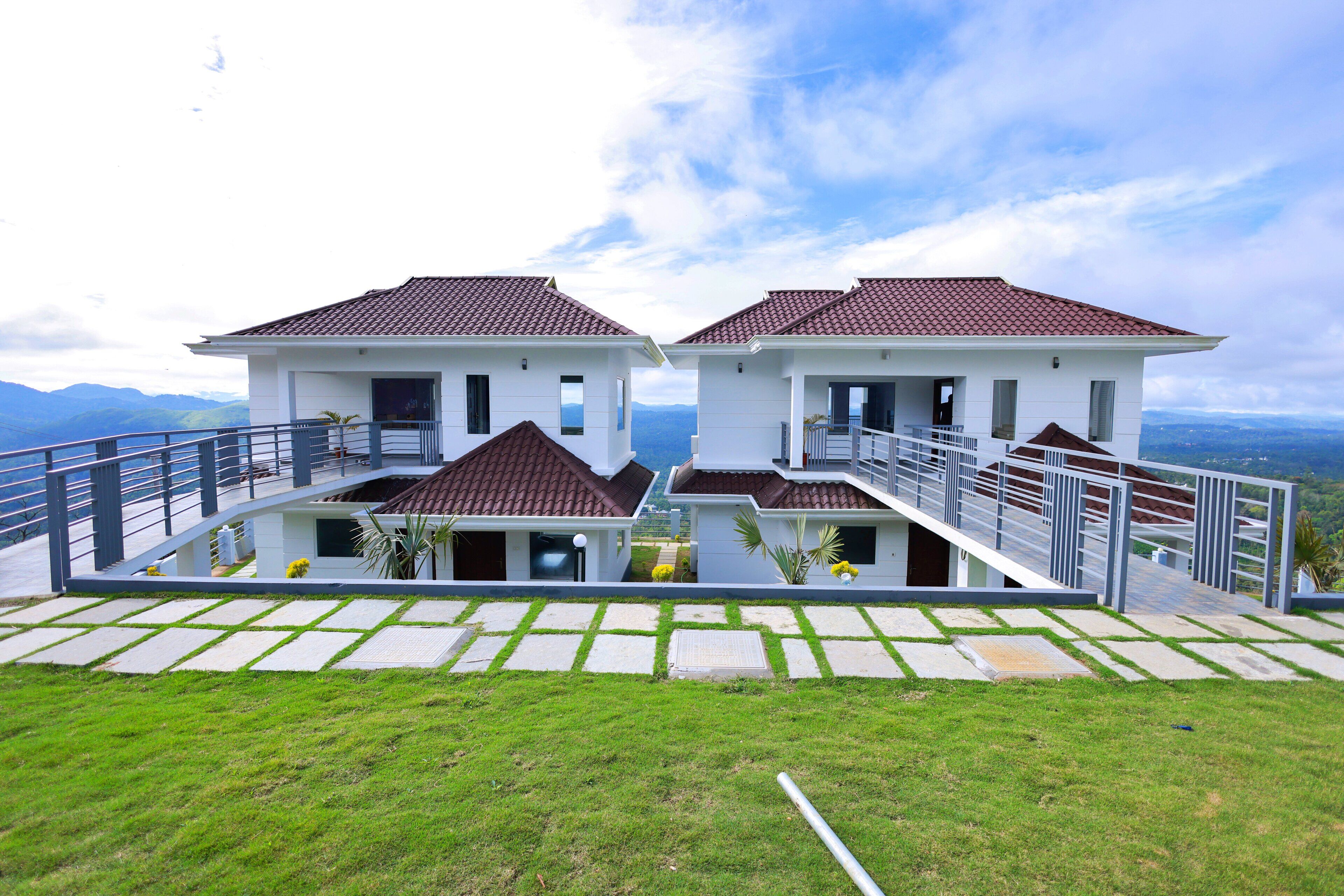 A modern two-story house with a balcony, a paved driveway, and a grassy lawn.