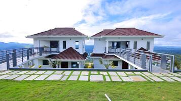 A modern two-story house with a balcony, a paved driveway, and a grassy lawn.