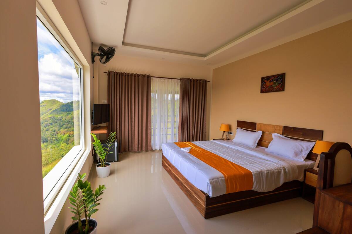 Ein Hotelzimmer mit einem großen Bett, einem Fernseher, einem Schreibtisch und einem Fenster mit Vorhängen.
