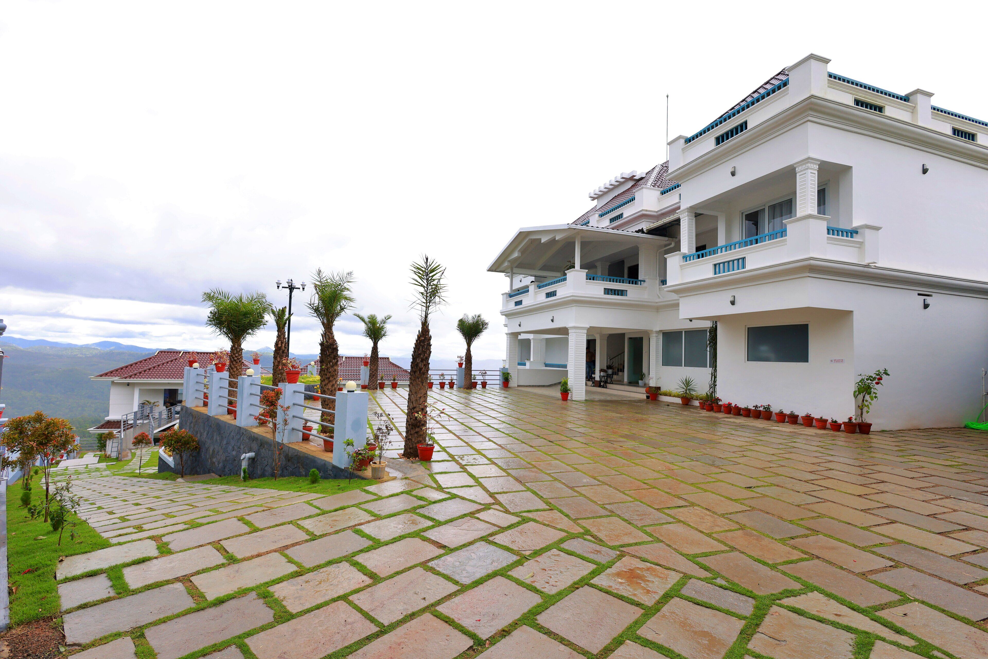 Un edificio moderno de dos pisos con un patio empedrado, varios balcones y vistas a las montañas.