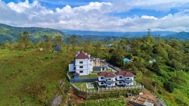 A large, multi-story building with a white facade and red roofs, surrounded by lush greenery and hills. - The Windy Mist Resort Munnar (Udumbanchola)
