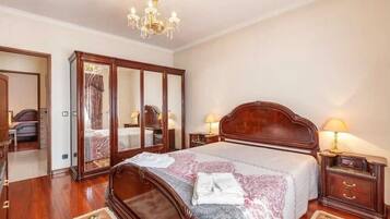 Een hotelkamer met een groot bed, een garderobe, een kroonluchter en een nachtkastje met een lamp.