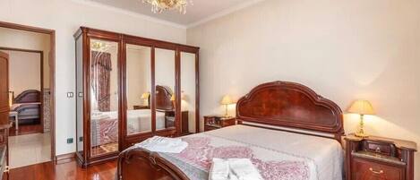 A bedroom with a large bed, wooden headboard, two bedside tables with lamps, a chandelier, and a large mirror.