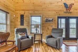 Cozy cabin-style room with a warm atmosphere, featuring two armchairs, a small table, and a wooden sign with a personal touch.