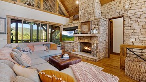 A cozy living room with a stone fireplace, a large sectional sofa, and a view of the outdoors. - Copperline Lodge - located in Blue Ridge, GA (Epworth)