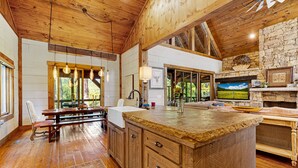 A rustic kitchen with wooden cabinets, a large island, and a stone wall. - Copperline Lodge - located in Blue Ridge, GA (Epworth)