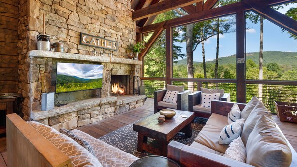 A stone fireplace with a TV, a wooden deck, and outdoor seating. - Copperline Lodge - located in Blue Ridge, GA (Epworth)