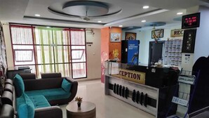 A reception area with a reception desk, seating area with sofas, and a digital clock. - Hotel Pavan Mansion (Raichur)