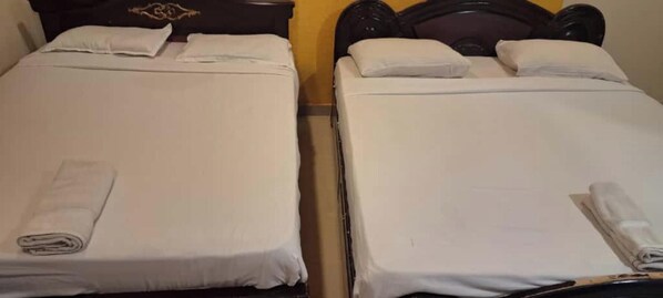 Two single beds with white linens and towels, wooden headboards, and a plain wall in the background.