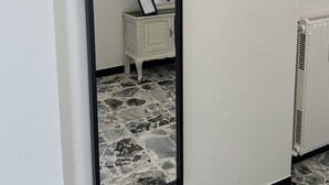 A mirror with a black frame, a small white side table with a picture frame, and a radiator on the floor. - Spacious and bright family apartment (Sestri Levante)