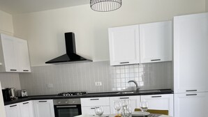 A modern kitchen with white cabinetry, a gas stove, and a dining table set for four. - Spacious and bright family apartment (Sestri Levante)