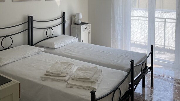 A bedroom with two beds, a nightstand, a lamp, and a window with curtains. - Spacious and bright family apartment (Sestri Levante)
