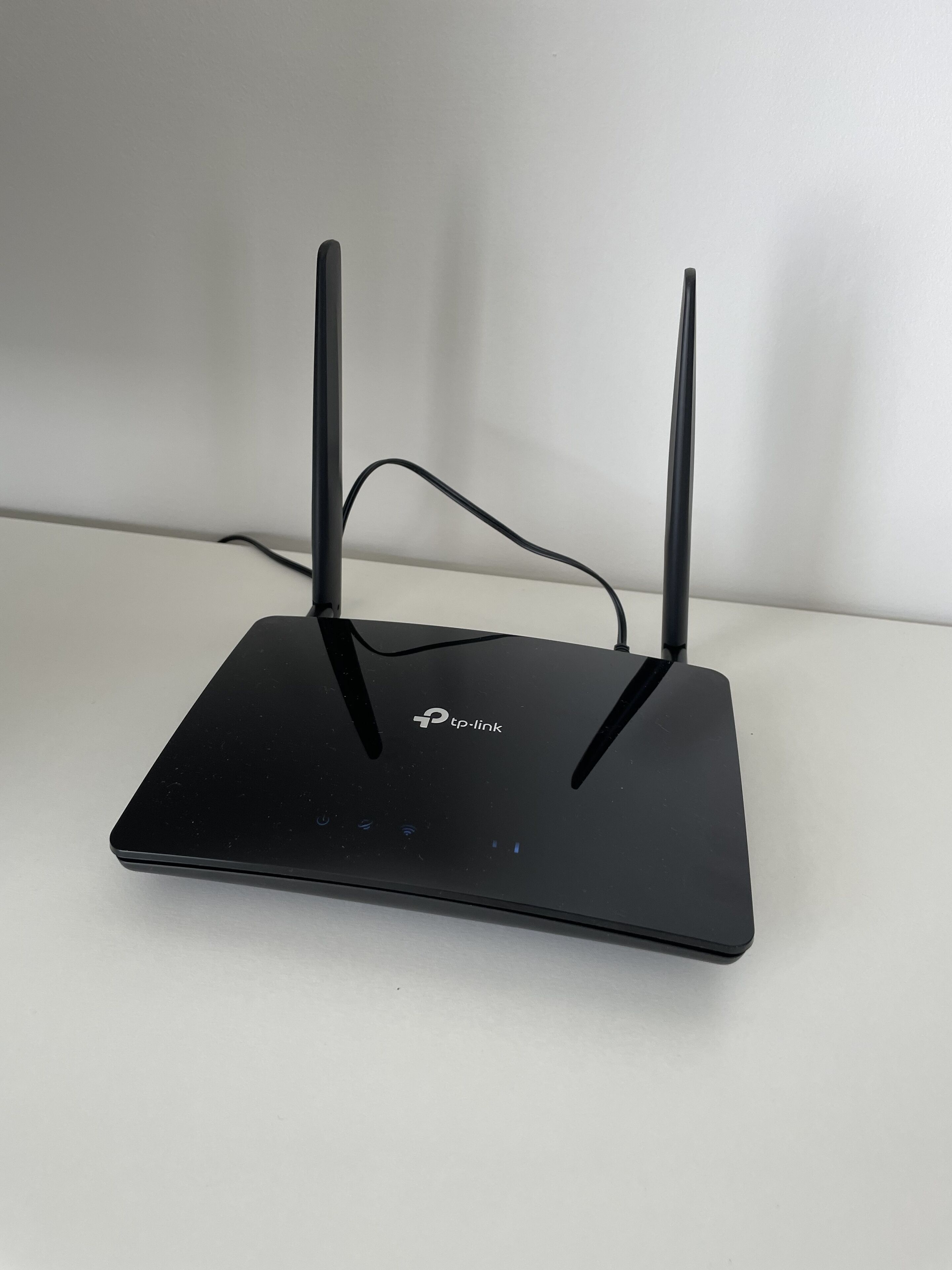 A black TP-Link router with two antennas on a white surface.
