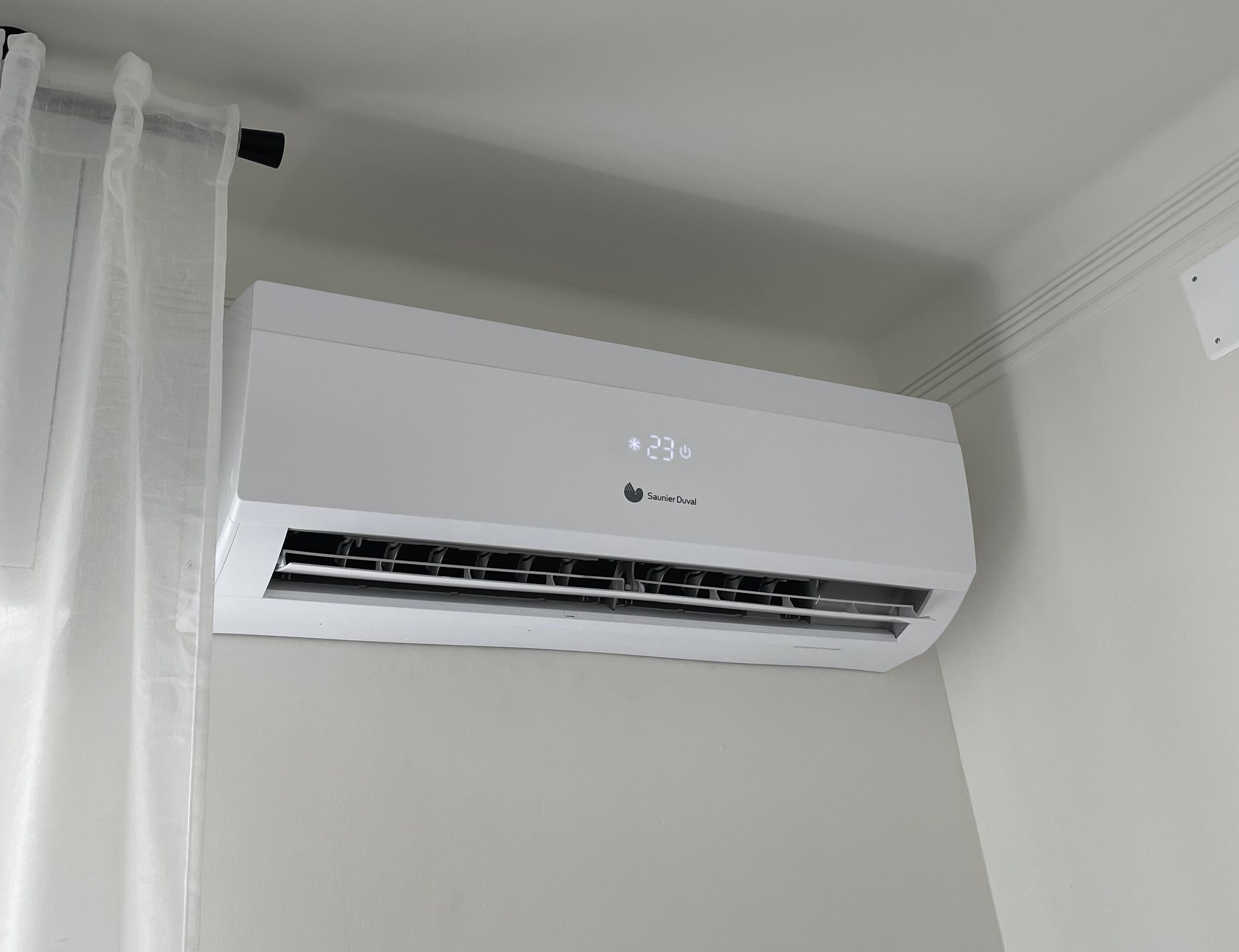 Un climatiseur blanc, fixé au mur, doté d’un écran numérique indiquant une température de 23 degrés.