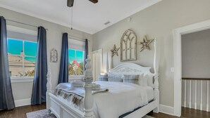 Ein Schlafzimmer mit einem weißen Bett, Blick ins Freie durch ein Fenster und einer Tür zu einem anderen Raum.