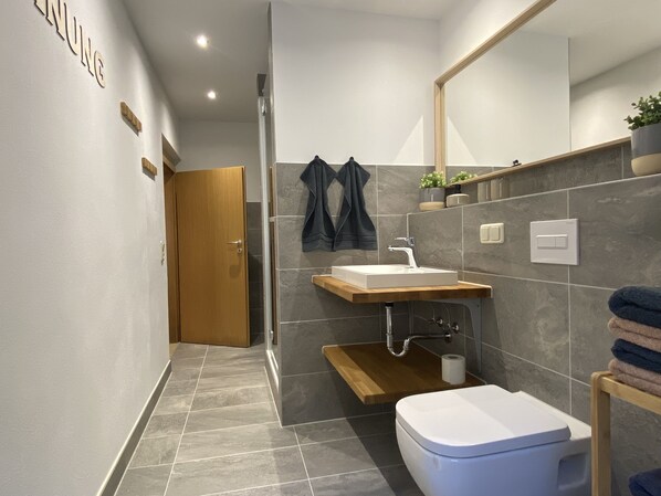 Une salle de bain moderne avec une porte en bois, un lavabo blanc, des toilettes et un espace douche.