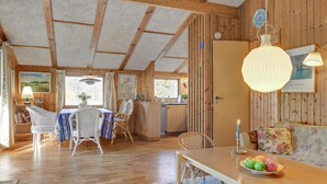 A cozy cabin interior with a dining area, kitchen, and a living space with a sofa and a table with fruit.