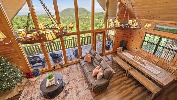 Ein gemütliches Blockhaus-Interieur mit einem großen Holzespeisetisch, einer bequemen Couch und Blick auf eine bewaldete Landschaft durch große Fenster.