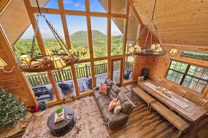 L’intérieur chaleureux d’un chalet avec une grande table à manger en bois, un canapé confortable et une vue sur un paysage boisé grâce à de larges fenêtres.