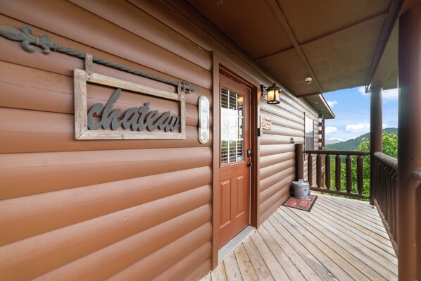 Une cabane en bois avec une pancarte sur la porte indiquant « château », une terrasse en bois et, en arrière-plan, une vue sur la verdure.