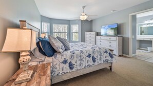 Une chambre à coucher avec un lit, une commode, une télévision et un ventilateur de plafond.