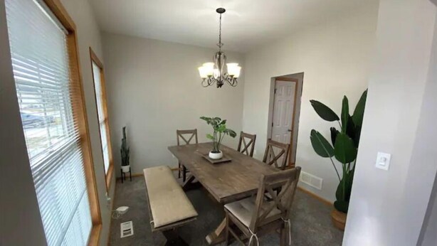 Une salle à manger avec une table en bois, des chaises, un banc, un lustre et une plante en pot.