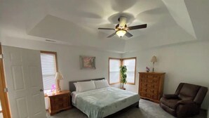 Une chambre à coucher comprenant un lit, une table de chevet, une chaise, une commode et un ventilateur de plafond.
