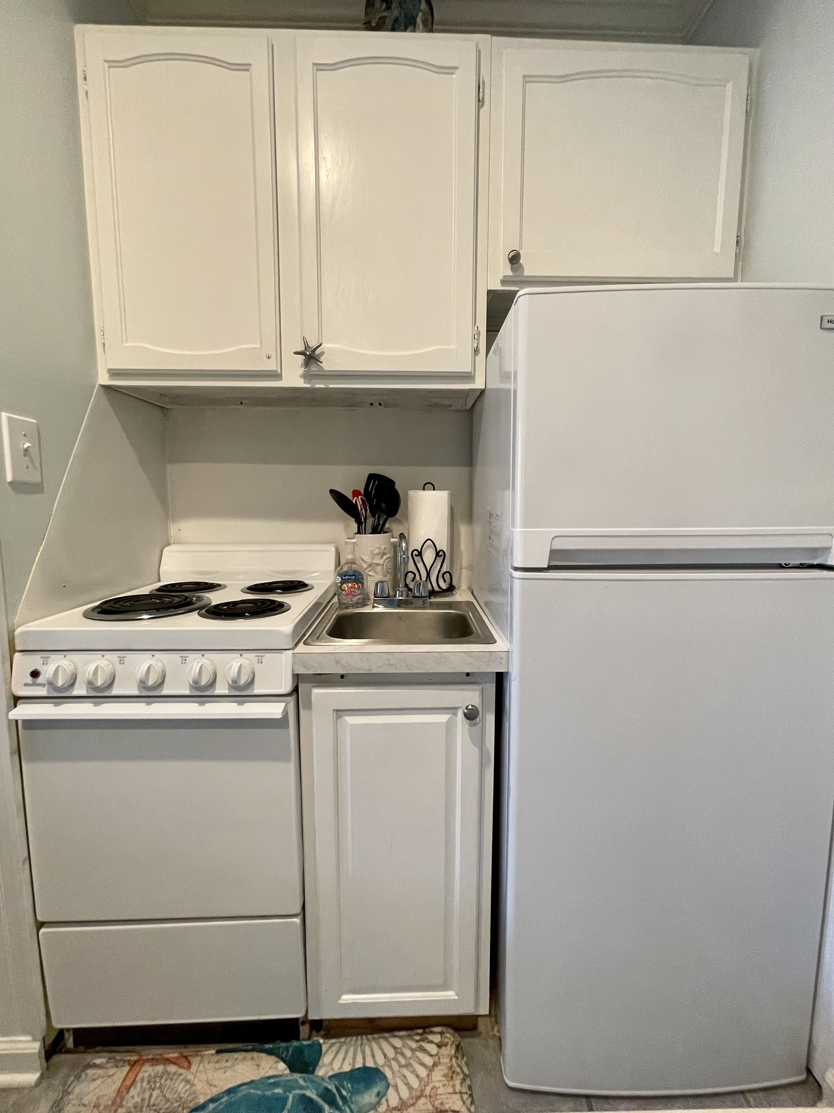 A compact kitchen with white cabinets, a stove, a sink, and a refrigerator.
