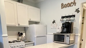A kitchen with white cabinets, a stove, a microwave, and a coffee maker. There are three green bar stools. - Oceanside, steps to the Beach, pets considered, cards avail, Beach Club Complex (Saint Helena Island)