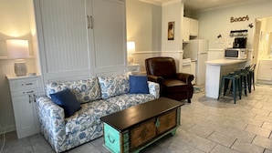 A living room with a patterned sofa, a brown leather chair, a wooden coffee table, and a kitchenette in the background. - Oceanside, steps to the Beach, pets considered, cards avail, Beach Club Complex (Saint Helena Island)