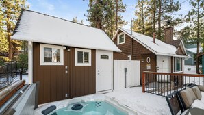 A hot tub with a wooden deck, a brown building with a white door, and a fenced area.
