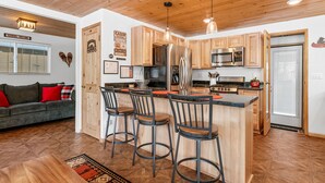 A modern kitchen with wooden cabinets, stainless steel appliances, and a bar area with stools.