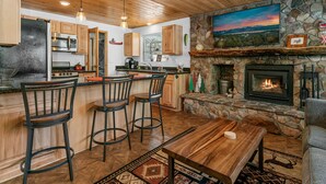 A kitchen with a stone fireplace, wooden ceiling, and a bar area with stools.