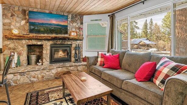 A cozy living room with a stone fireplace, a large window, and a view of the outdoors.