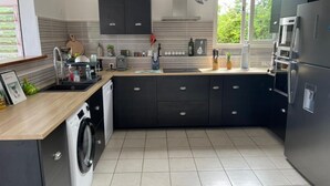A modern kitchen with a built-in washing machine, a large refrigerator, and a window providing natural light. - Villa rouge les p'tits noirmoutrins saint François  (Saint-François)