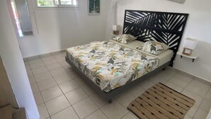 A bedroom with a bed, a window, a wall-mounted air conditioner, and a ceiling fan. - Villa rouge les p'tits noirmoutrins saint François  (Saint-François)