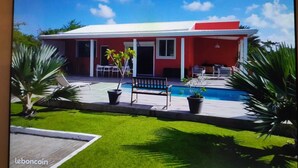 A modern house with a red exterior, a swimming pool, and a well-maintained lawn. - Villa rouge les p'tits noirmoutrins saint François  (Saint-François)