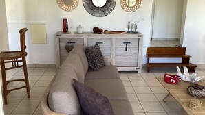 A living room with a wooden sofa, a wooden chair, a wooden bench, and a dining table with a red bowl and a decorative item. - Villa rouge les p'tits noirmoutrins saint François  (Saint-François)
