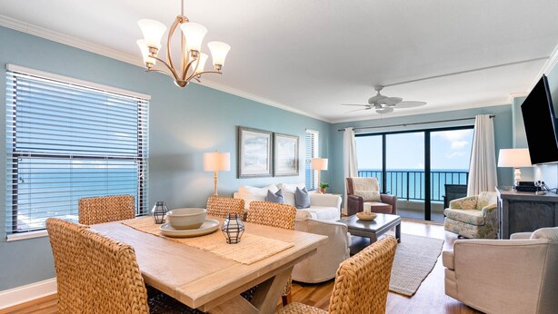 A spacious living room with a dining area, wicker furniture, a chandelier, and a large window with a view.