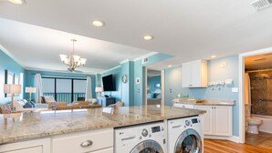 A laundry area with two front-loading washing machines, a countertop with a sink, and a mirror above the machines.