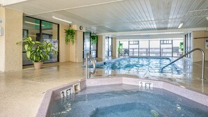 An indoor swimming pool with a hot tub, potted plants, and a clock on the wall.