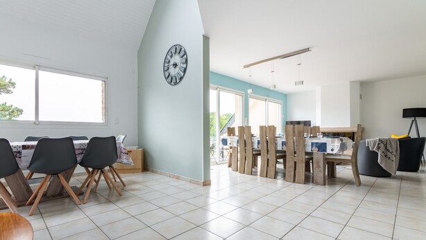 Une salle à manger spacieuse avec un plafond haut, de grandes fenêtres et une horloge au mur.